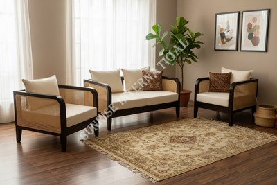 A styled living room set featuring a cream and cane armchair, a matching sofa, and a second armchair with patterned accent pillows, arranged around a carved wooden coffee table on a traditional rug.