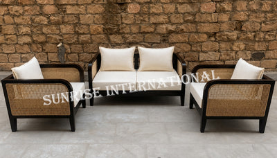 Three-piece outdoor patio furniture set including a three-seat sofa, two armchairs, with black frames, woven cane panels, and cream cushions, set against a rustic brick wall.