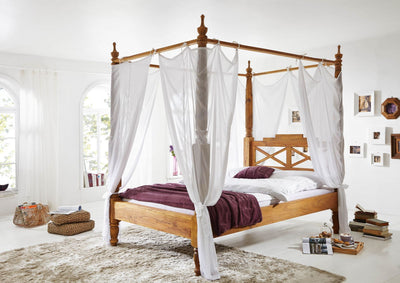 Wooden four poster bed with hand-carved posts and curtains, angled bedroom view