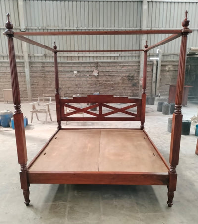 Hand-carved wooden four poster bed frame with tall posts, front workshop view