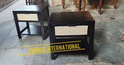 Two black Sheesham wood bedside tables featuring a single drawer with natural rattan cane detailing and an open lower shelf.