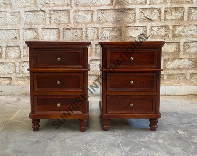 A pair of dark reddish-brown wooden three-drawer nightstands with brass knobs, positioned side-by-side against a light stone brick wall.